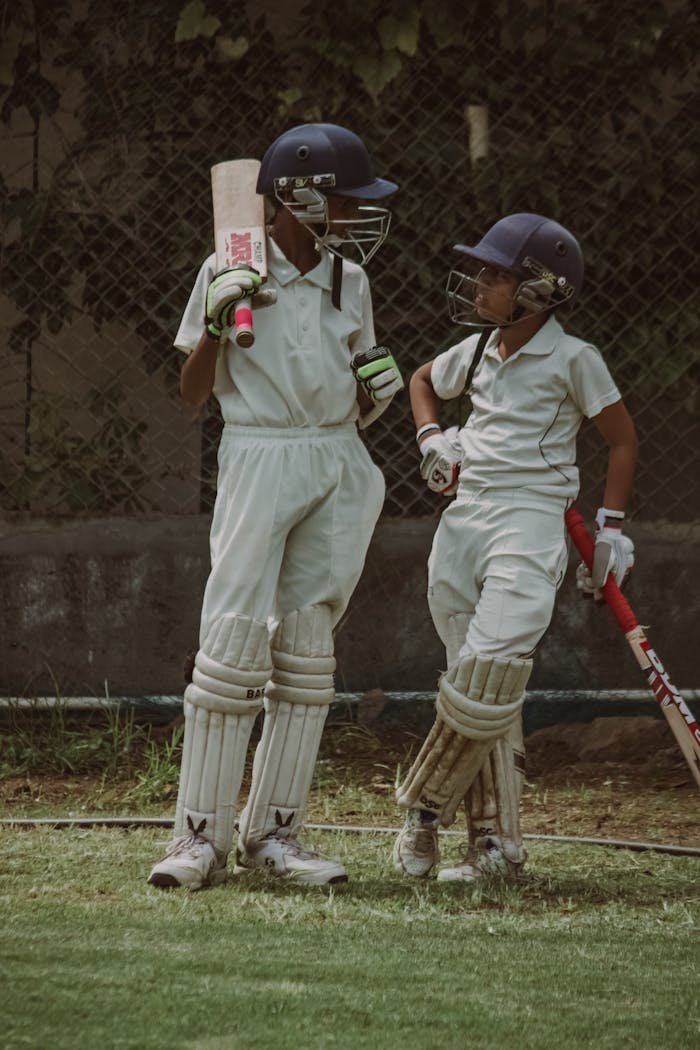 services-02 Two young cricketers in full gear discussing strategy on the field in Gahunje, India.