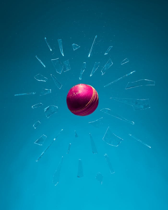 services-04 Dynamic shot of a red cricket ball breaking through glass against a teal backdrop.